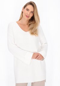 Fehér kötött pulóver V-nyakkal, hosszú ujjal és laza szabással. Texturált anyagú, enyhén ívelt hem elejével rendelkezik.