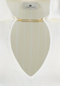 Top bianco a costine con scollo profondo a V e dettaglio in metallo dorato sul collo con un accento di cristallo. Sottile motivo a righe verticali.