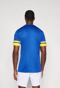 Maglia sportiva blu con accenti gialli e strisce sulle maniche, realizzata in tessuto liscio, con scollo rotondo e maniche corte.