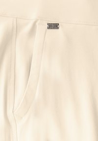 Beige joggers gemaakt van zachte stof met een elastische tailleband, voorzien van een voorkantzak en een zilver kleurenaccent nabij de tailleband.