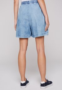 Pantalones cortos de mezclilla en azul claro con una cintura elástica, que presentan un corte relajado y costuras visibles. Combinados con zapatillas azul marino.
