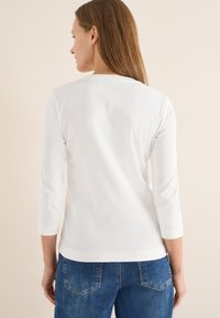 Haut blanc côtelé à manches trois-quarts. Présente un col rond et un ourlet droit. Associé à un jean en denim foncé.