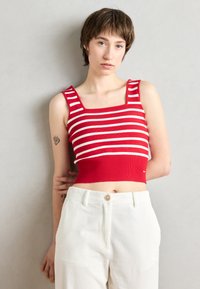 Crop top rayé rouge et blanc avec un décolleté carré et une texture côtelée, associé à un pantalon large en velours côtelé de couleur écru.