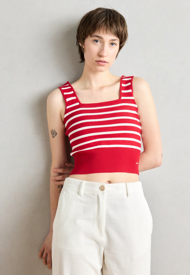 Crop top rayé rouge et blanc avec un décolleté carré et une texture côtelée, associé à un pantalon large en velours côtelé de couleur écru.