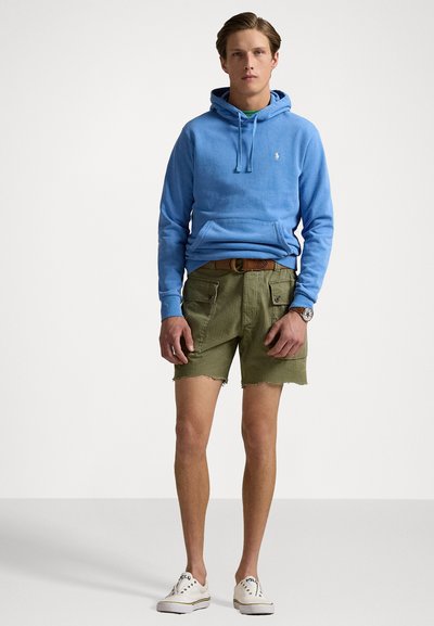 Lys blå bomulds-Hoodie med en frontlomme, parret med olivengrønne shorts og hvide sneakers. Enkel design, afslappet pasform og afsluttede ærmer.