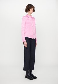 Pink snake-patterned button-up shirt with two chest pockets, paired with dark denim wide-leg pants and black ankle boots.