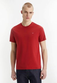 Camiseta roja de manga corta hecha de algodón. Presenta un cuello redondo y un pequeño logo blanco en el lado izquierdo del pecho. Textura suave, corte relajado.
