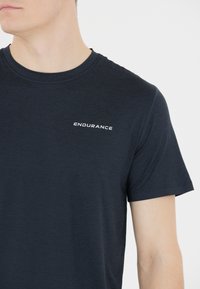 Granatowa koszulka z krótkim rękawem wykonana z miękkiej tkaniny, z białym logo "ENDURANCE" na lewej piersi, okrągłym dekoltem i regularnym krojem.