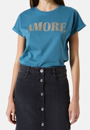 Bawełniany t-shirt w kolorze zielononiebieskim z krótkimi podwiniętymi rękawami i złotym napisem "AMORE", zestawiony z czarną spódnicą dżinsową zapinaną na guziki z przodu.