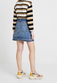 Džínová sukně s třepícími se okraji, střední odstín, dvě zadní kapsy. Kombinována s pruhovaným svetr a vícolorovými teniskami.