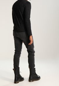 Czarna longsleeve z wzorem w drobne kropki, zestawiona z ciemnoszarymi dżinsami i czarnymi sznurowanymi botkami na płaskiej powierzchni.