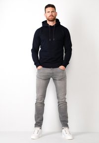 Sudadera marina con cordones, combinada con jeans gris claro y zapatillas blancas. Diseño ajustado, textura suave, marca mínima en la prenda.