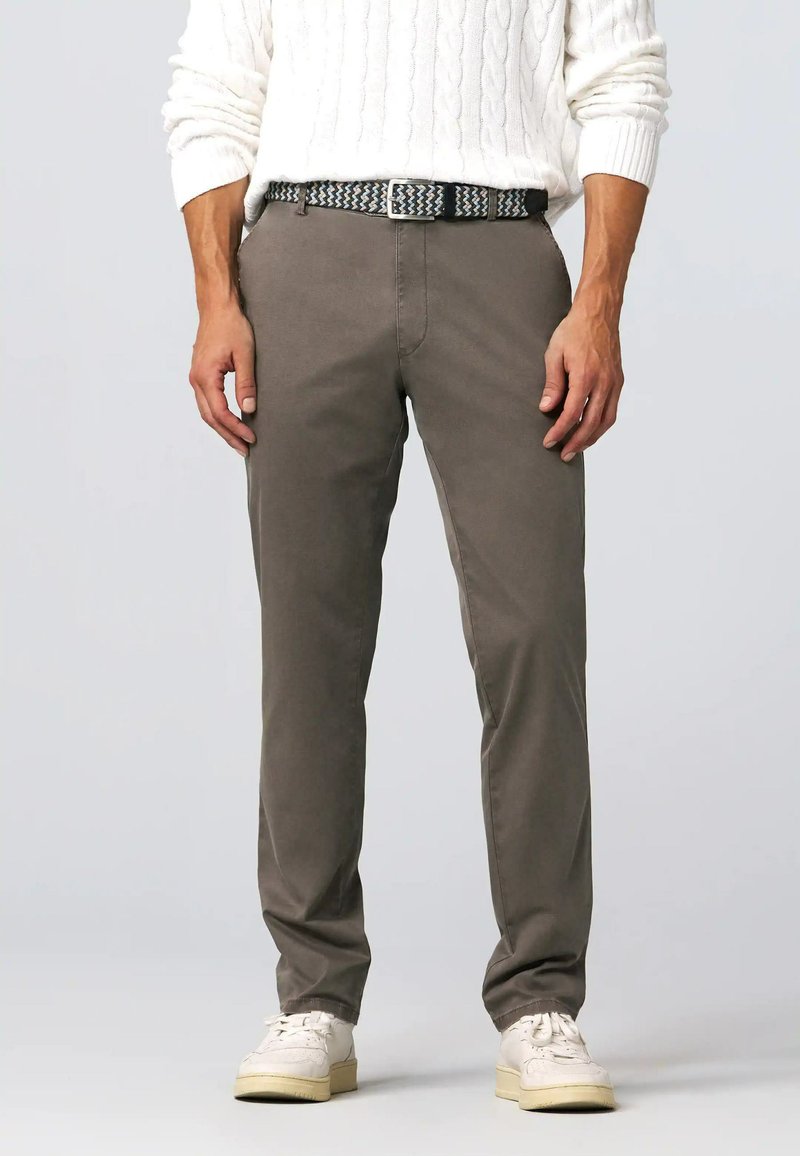 Chinos khaki in cotone con pancia piatta, gambe dritti e tasche visibili; abbinati a una cintura con motivo e scarpe da ginnastica bianche.