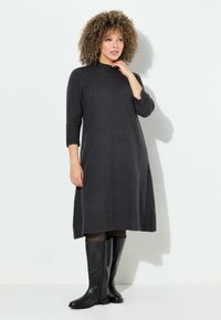 Tummanharmaa neulemekko, jossa on korkea kaulus ja kolmanneksen pituiset hihat. Mekko on löysä ja se ulottuu polven ylle. Yhdistetty mustiin polvipitkiin saappaisiin.