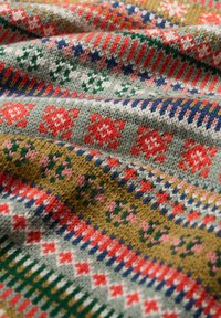Gebreid textiel met ingewikkelde patronen in rood, groen, blauw en roze op een grijze en olijfgroene achtergrond. Zachte textuur en verschillende ontwerpen.