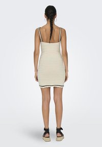 Knit dress in cream with black accents, form-fitting design, scoop back, and adjustable straps. Paired with black strappy espadrilles.