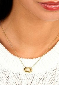 Goldene Halskette mit einem ovalen Anhänger, der eine Perle hält, vor einem weißen gestrickten Pullover präsentiert. Die Kette ist zart und fein.