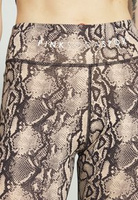 Legíny s vysokým pasem s béžovým a hnědým hadím vzorem, vyrobené z hladkého, pružného materiálu s viditelnými švy.