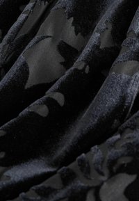 Tissu noir avec des motifs floraux en velours en relief créant texture et ombres sur une surface doucement pliée.
