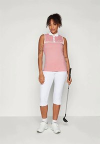 Rožinė be rankovių polo marškiniai su baltais akcentais ir mygtukais, derinami su baltais trumpais kelnais. Aprangą papildo balti sportiniai bateliai ir golfo lazdas.