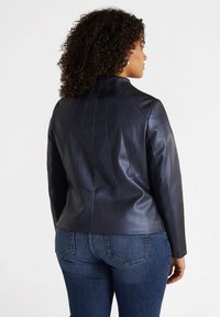 Navy leather jacket with a fitted design, high collar, and vertical seam detailing on the back, paired with blue jeans.