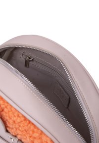 Interno di una borsa color beige chiaro che presenta un morbido rivestimento in fleece arancione, una tasca con zip e un rivestimento grigio con un'etichetta del marchio visibile.