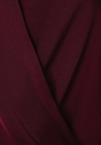 Tessuto borgogna con una superficie liscia, leggermente riflettente e pieghe cadenti, che indicano un materiale leggero.