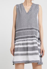 Vestido sin mangas con escote en V, hecho de tela estampada en blanco y negro, con diferentes diseños de rayas y un dobladillo con volantes.