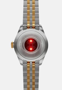 Edelstahlarmbanduhr mit doppeltem Armband in zwei Farben, goldenen Akzenten, beleuchteten Sensoren und graviertem Gehäuseboden mit Modelldetails.