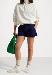 Laivastonsiniset shortsit, vaalean kermanvärinen pusero, jossa on kaulus ja napit, vihreä käsilaukku sekä valkoiset korkeavyötäröiset tennarit beigeillä sukilla. Yksinkertainen muotoilu ja värit.