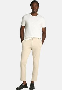 Pantaloni tapered beige e una maglietta a girocollo grigio chiaro. L'outfit è completato da mocassini neri. Il tessuto appare liscio con una vestibilità casual.