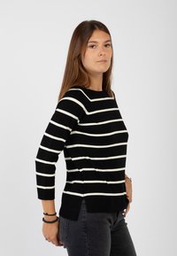 Maglione a righe bianco e nero con scollatura rotonda e maniche a tre quarti. Presenta un motivo a tricot testurizzato e fessure laterali all'orlo.