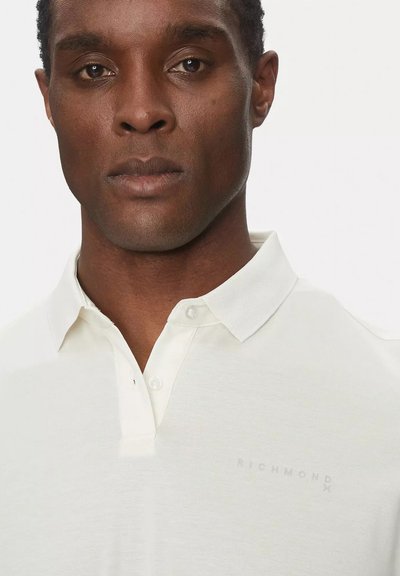 Polo bianco con colletto a tre bottoni, realizzato in tessuto morbido. Presenta un logo "RICHMOND" grigio chiaro sul petto.