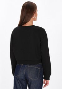 Fekete, rövidített pulóver kerek nyakkal és hosszú ujjakkal, puha anyagból készült. Kék farmernadrággal párosítva, laza, kényelmes viseletet nyújt.