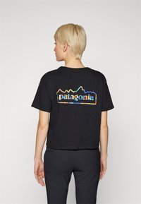 Juodas trumpas T-shirt'as su daugiaspalviu „Patagonia“ logotipu ir kalnų grafika nugarinėje pusėje. Minkšta medvilnė, laisvas fasonas.