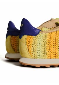 Zapatillas deportivas con una parte superior trenzada multicolor en amarillo y verde, con detalles de cuero suave en azul y una suela de goma beige.