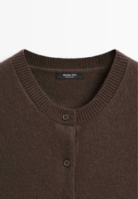 Cardigan en maille marron avec un col rond et deux boutons foncés, montrant l'étiquette de la marque "Massimo Dutti" à l'intérieur du col.