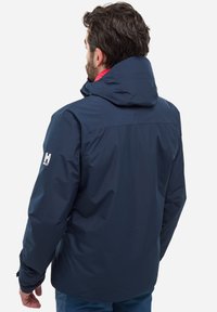 Navy blue waterproof jacket with a hood, featuring a smooth texture and elastic cuffs. Notable logo on the left sleeve.