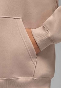 Jasnoróżowy sweatshirt z kieszenią z przodu, prążkowanymi mankietami i gładką teksturą materiału, z widocznymi detalami szwów i luźnym krojem.