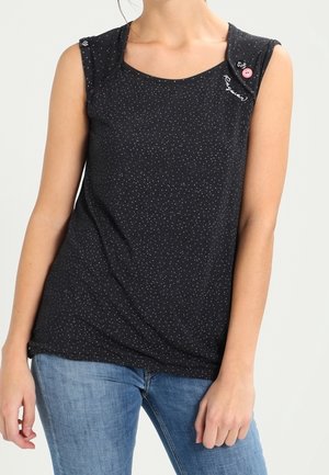 Vrouw die een mouwloos zwart shirt draagt met kleine witte stippen, knoopdetails op de schouders en lichtblauwe spijkerbroek.