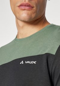 T-shirt nera e verde con collo a giro, texture morbida e logo bianco "Vaude" sul petto. Design con blocchi di colore a contrasto.