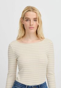 Beige långärmad topp med horisontella ljusbruna ränder, rund halsringning och ribbad textur, kombinerad med blå denimjeans.