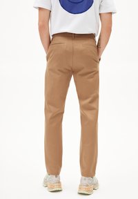 Chinos marron clair avec une coupe droite, dotés de poches arrière et d'un tissu lisse. Portés avec un t-shirt blanc et des baskets.