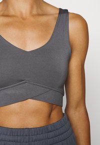 Grauer, taillierter Croptop mit V-Ausschnitt, nahtlosen Kanten und gekreuztem Vorderteil, aus weichem, dehnbarem Material.