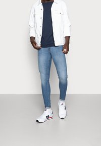 Chaqueta de mezclilla blanca, camiseta navy, vaqueros skinny de color azul claro y zapatillas blancas con acentos en rojo y navy. Textura suave, diseño casual.
