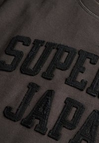 Ciemnoszara bluza z dużym, czarnym haftowanym napisem "SUPER JAPAN", z teksturowanym wykończeniem i prążkowanym dekoltem.
