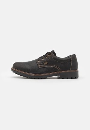 Chaussure en cuir noir avec un bout arrondi, un laçage, une couture contrastante en marron, une semelle en caoutchouc et une finition en matériau texturé.