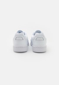 Fehér sportcipő sima bőr felsőrésszel, texturált kiegészítőkkel a saroknál, és a "Reebok" felirattal a hátsó részen. Lapos gumitalp.