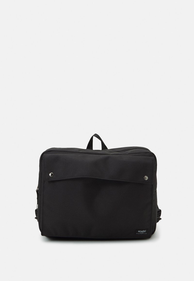 Svart canvasryggsäck med en framficka, två silverfärgade tryckknappar, handtag upptill och justerbara axelremmar. Slät textur.