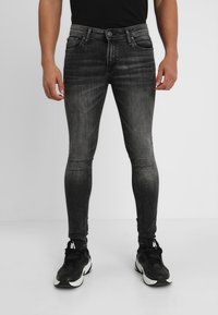 Jeans skinnys negros con un lavado gris descolorido, que cuentan con cinco bolsillos y una cremallera, combinados con zapatillas deportivas negras.